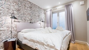 Ein modernes Schlafzimmer mit einem großen Bett, einem Nachttisch, einer Lampe und einem Fenster mit Vorhängen.