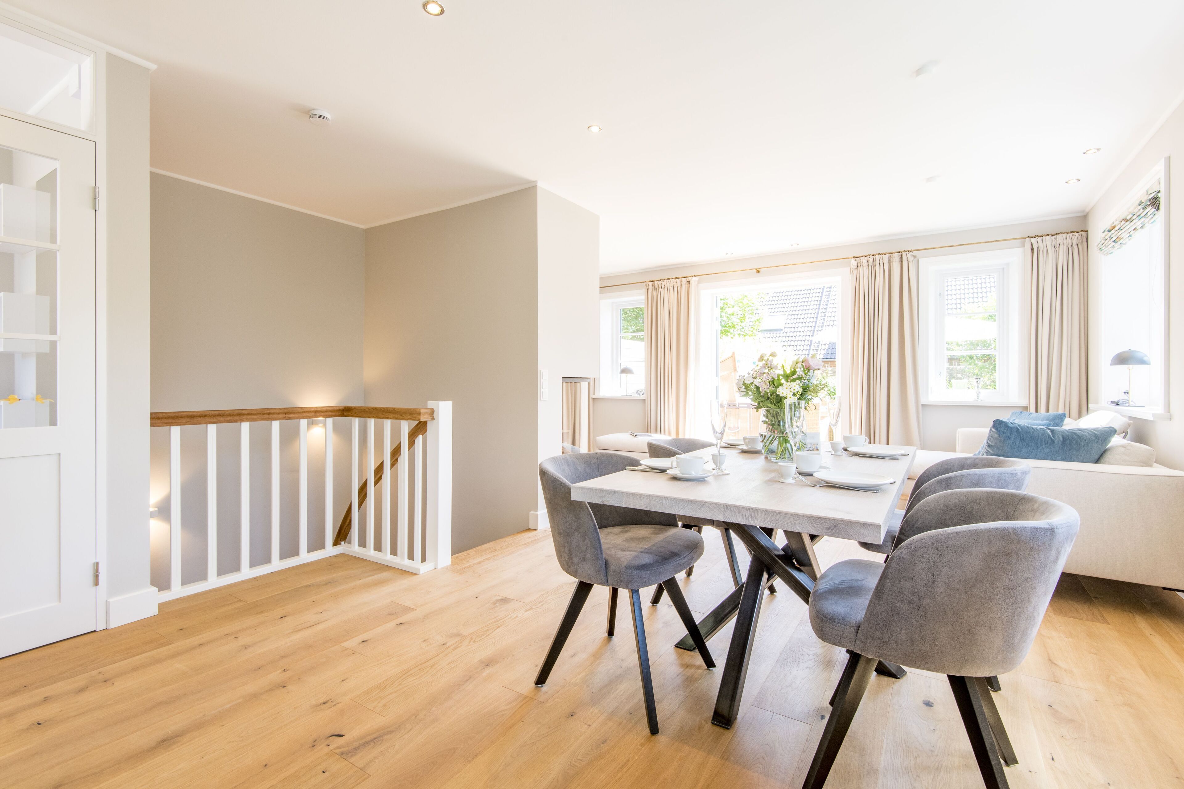 Une salle à manger spacieuse avec un plancher en bois, une table blanche et des chaises recouvertes d’un tissu gris.