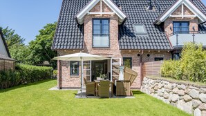 Ein zweistöckiges Haus mit Backsteinfassade, einem Ziegeldach und einer Steinmauer im Hinterhof. Es gibt eine Terrasse mit Gartenmöbeln und einen überdachten Sitzbereich.
