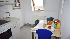 Ett kök med vita skåp, en spis, ett fönster med utsikt och ett frukostbord med olika sorters mat och dryck.