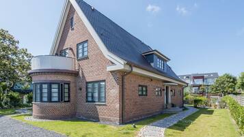 Ein zweistöckiges Backsteinhhaus mit geneigtem Dach, einer kreisförmigen Auffahrt und einem Kiesweg, der zum Eingang führt.