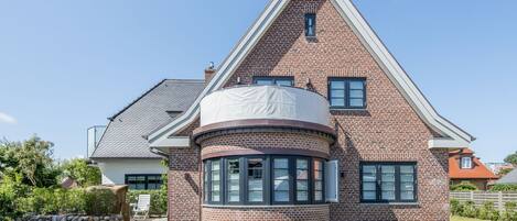 Une maison à deux étages, avec une façade en briques, une fenêtre ronde et un toit en pente.