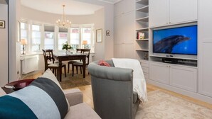 Ett vardagsrum med en grå soffa, en matplats med en kristallkrona och en tv-skärm som visar en delfin.