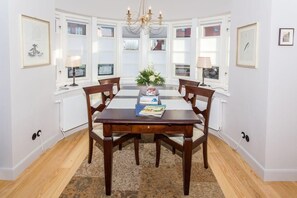 A dining room with a wooden table, six chairs, a chandelier, and a window with blinds.