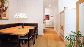 Un coin repas avec une table et des chaises en bois, un lustre et un tableau représentant des fruits accroché au mur.