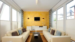 Un salon moderne avec deux canapés, une table basse, un téléviseur fixé au mur et de grandes fenêtres.