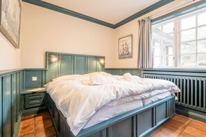 A bedroom with a single bed, a nightstand, a window with curtains, and a radiator.