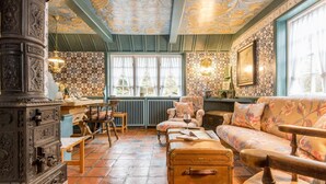 A room with a vintage aesthetic, featuring a wooden cabinet, a sofa, a chair, a table, and a window with curtains.