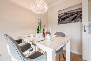 Een eetruimte met een witte tafel gedekt voor vier personen, een kroonluchter en een zwart-wit foto aan de muur.