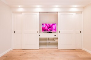 Een kamer met een witte garderobe, een televisie op een standaard en een houten vloer.