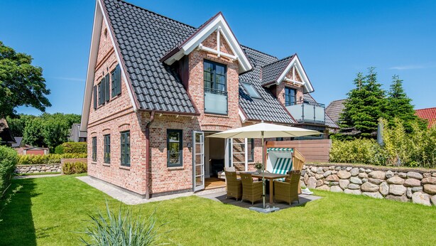 Een twee verdiepingen tellend huis met een bakstenen gevel, een hellend dak en een stenen muur rondom het terrein.
