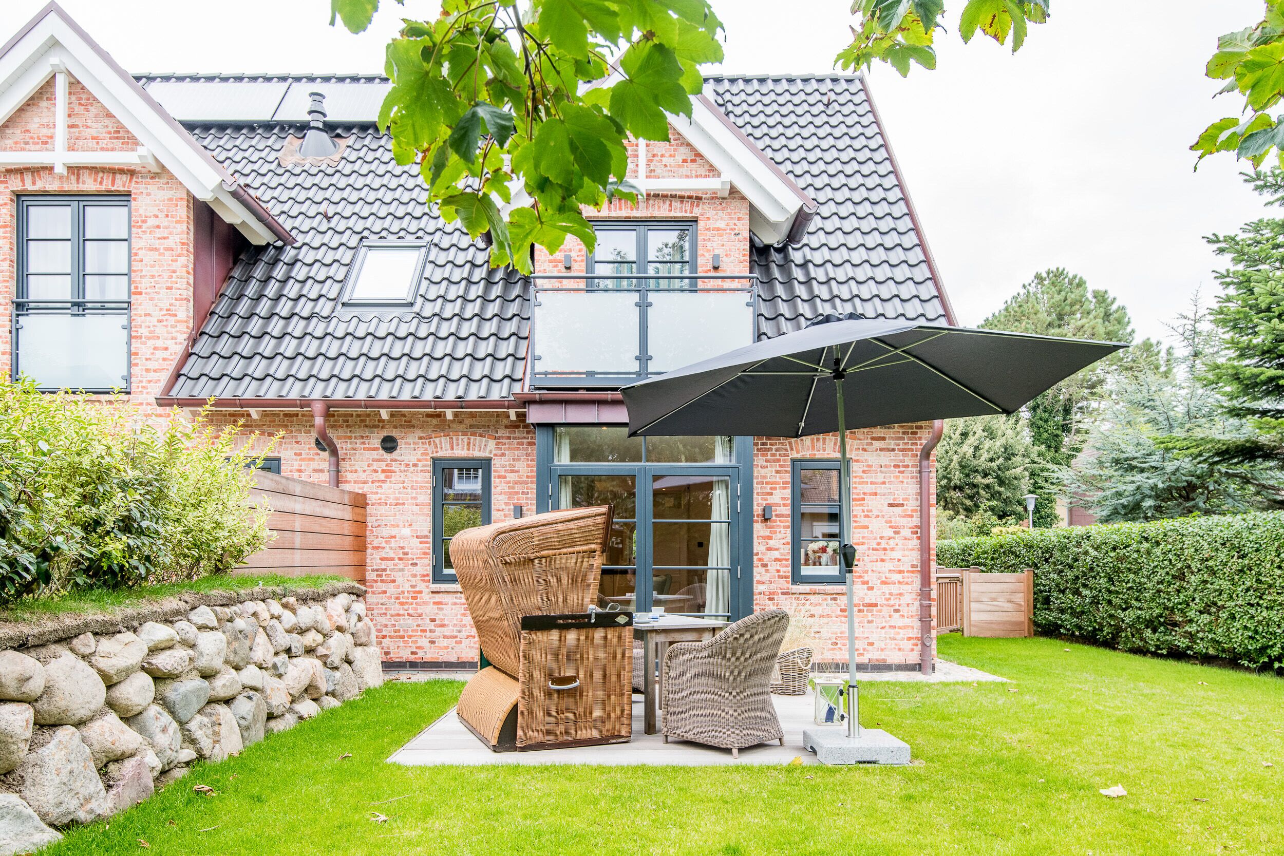 A brick house with a tiled roof, a stone wall, and a grassy lawn.