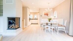 Een moderne keuken met witte kasten, een eetgedeelte met witte stoelen en een open haard met hout.