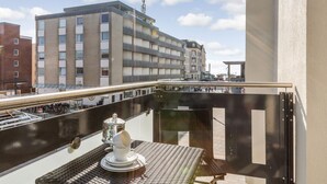A balcony with a table and a cup, overlooking a cityscape with buildings and a clear sky. - Art your Life - Residence, Whg. 3 Romero (Westerland)