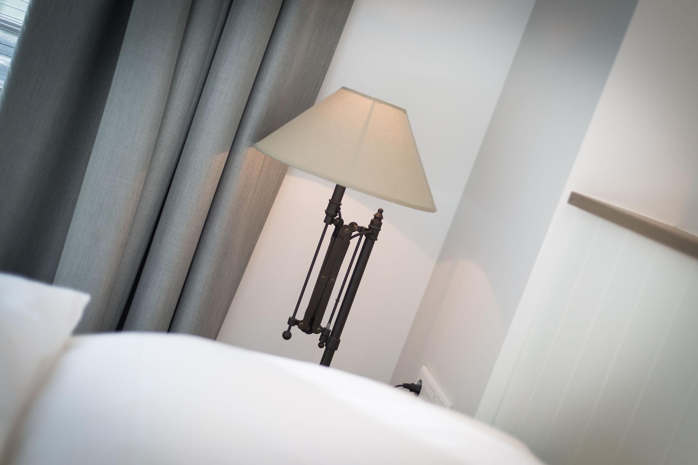A hotel room with a bed, a lamp, and curtains.