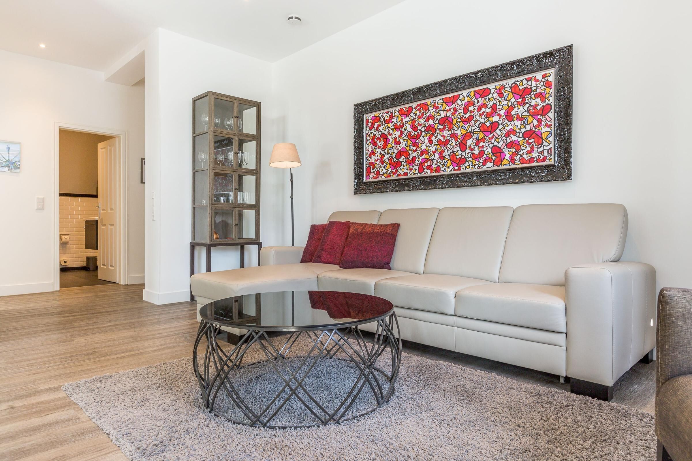 Una sala de estar moderna con un sofá blanco, una mesa de centro de vidrio y un cuadro abstracto rojo en la pared.