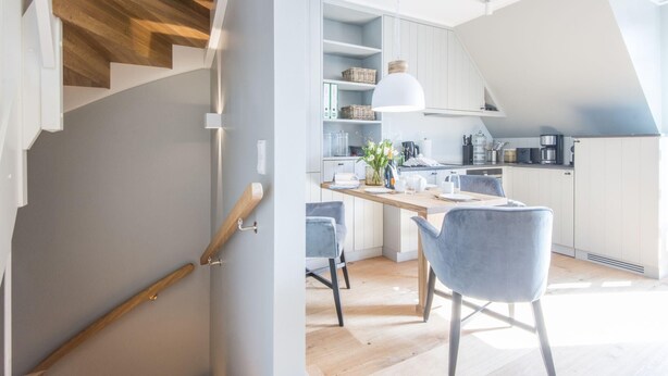 A modern kitchen with white cabinets, a wooden staircase, and a dining area with two chairs. - Exquisit. Wellness. Balkon. Höög Hüs, Whg. 2A Objekt-id: Whw/02a (Westerland)