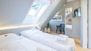 Ein modernes Schlafzimmer mit Dachfenster, einem Bett mit weißer Bettwäsche, einem Sessel und Bildern an den Wänden.