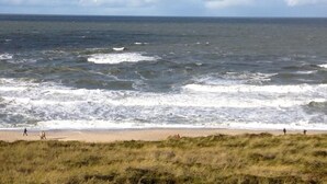 A beach with waves crashing onto the shore and a grassy area in the foreground. - Exquisit. Wellness. Balkon. Höög Hüs, Whg. 2A Objekt-id: Whw/02a (Westerland)