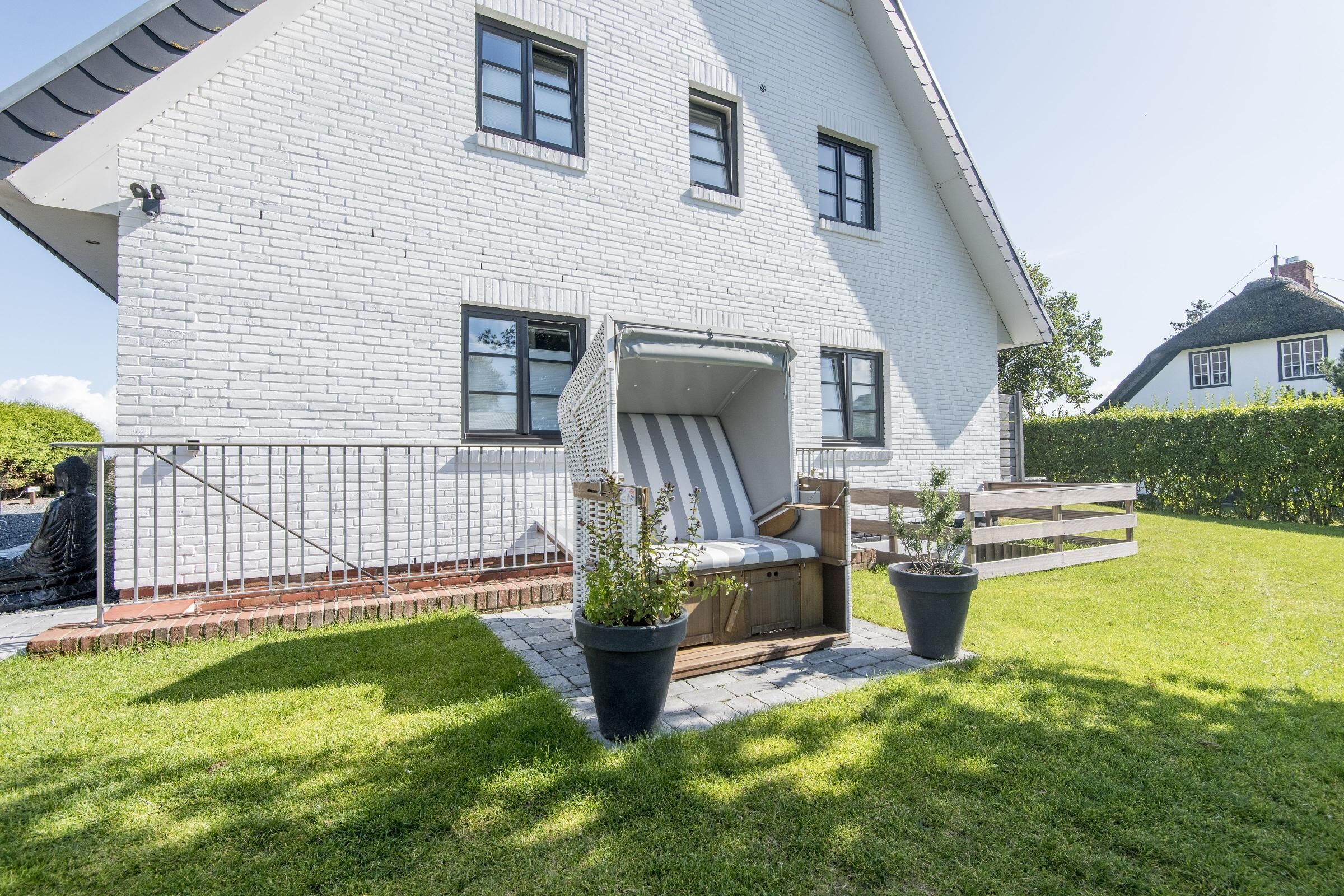 Ett vitt tegelhus med ett sluttande tak, en täckt uteplats och en liten trädgård med krukväxter.