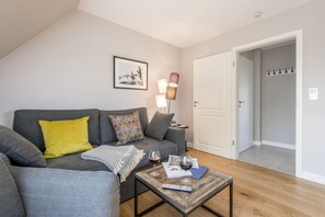 A living room with a grey sofa, a coffee table with a remote control, wine glasses, and a lamp.