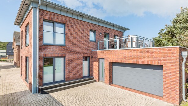 Un bâtiment moderne à deux étages, doté d’une façade en briques, de grandes fenêtres et d’un garage couvert.