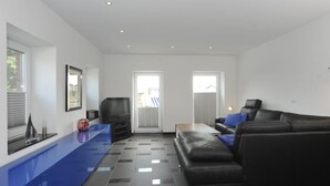 Un salon moderne avec un canapé en cuir noir, un mur d’accent bleu et un téléviseur à écran plat.