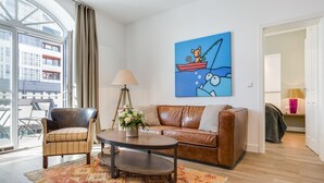 Ein modernes Wohnzimmer mit einem Ledersofa, einem braunen Sessel und einem Couchtisch. Ein großes Fenster bietet Blick auf die Stadt.