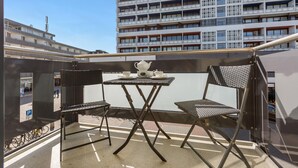 Ein Balkon mit Tisch, der für Tee gedeckt ist, zwei Stühlen und Blick auf ein Hochhaus.