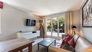 Ein Wohnzimmer mit einer Couch, einem Couchtisch, einem an der Wand befestigten Fernseher und einer Glasschiebetür zu einem Außenbereich.