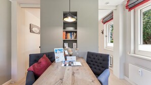 Ein Essbereich mit Holztisch, zwei Stühlen, einer Pendelleuchte, einem Bücherregal und einem Fenster mit Vorhängen.