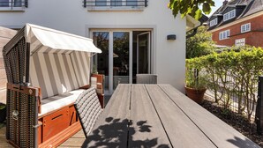 Eine Terrasse mit Holztisch und -stühlen, einem weißen Sonnensegel und einem Blumentopf.