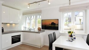 A modern kitchen with white cabinets, a built-in oven, a large window with a view, and a dining area with a table and chairs. - Strandnah. Ruhig. Komfortabel. Objekt-id: Hdr/04 (Westerland)