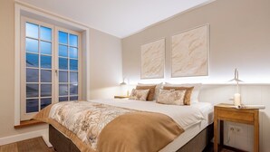 Ein Schlafzimmer mit einem großen Bett, einem Nachttisch, einer Lampe und einem Fenster mit Blick.