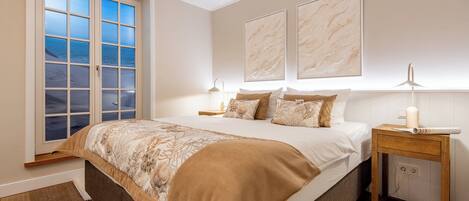 A bedroom with a large bed, a nightstand, a lamp, and a window with a view.
