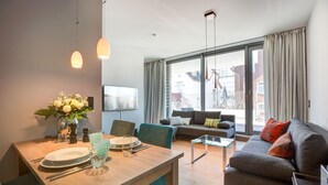 A modern living room with a dining table set for two, a sofa, and a large window with curtains. - Modern. Apart. Lichtdurchflutet. Neue Mitte, Whg. 4 Objekt-id: Nmw/04 (Westerland)