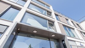 A modern building facade with large windows, a prominent elevator, and a visible door with a number. - Modern. Apart. Lichtdurchflutet. Neue Mitte, Whg. 4 Objekt-id: Nmw/04 (Westerland)