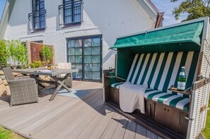 Eine Terrasse mit Tisch und Stühlen, ein gestreiftes Outdoor-Sofa und ein weißes Haus im Hintergrund.