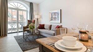A modern living room with a sofa, coffee table, and dining table set with plates and glasses. - Strandnah. Meerblick. Wellness (Westerland)
