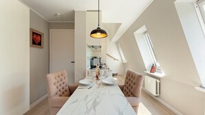 Un comedor con una mesa de mármol, dos sillas acolchadas, una lámpara colgante y vista a la cocina al fondo.