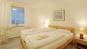 Een hotelkamer met twee bedden, een raam met gordijnen, een aan de muur hangend schilderij en bedlampjes.