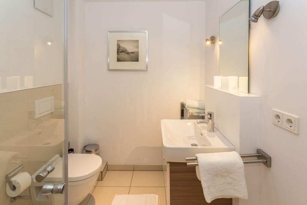 A modern bathroom with a glass shower enclosure, a white toilet, a sink with a towel rack, and a framed picture on the wall.