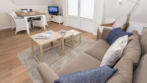 Een moderne woonkamer met een bank, een salontafel, een eettafel met stoelen, een televisie en een raam met zonwering.