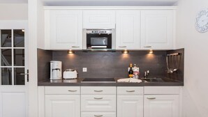 Een moderne keuken met witte kastjes, een inbouwoven, een koffiezetapparaat en een fles wijn.
