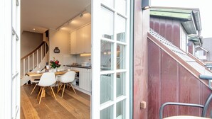 Una cocina moderna con armarios blancos, una zona de comedor con mesa y sillas de madera, y una escalera que sube a un nivel superior.