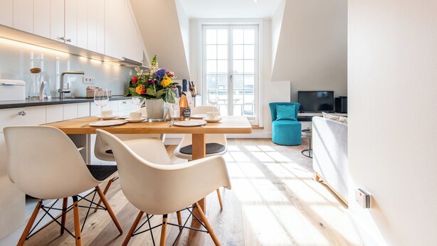 Una cocina moderna con armarios blancos, una mesa de comedor de madera y dos sillas blancas.