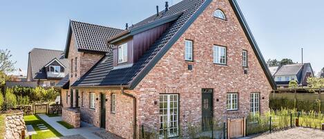 A brick house with a sloped roof, a front porch, and a gravel driveway.
