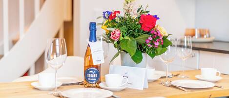 A dining table set with plates, cutlery, a bottle of wine, and a floral centerpiece.