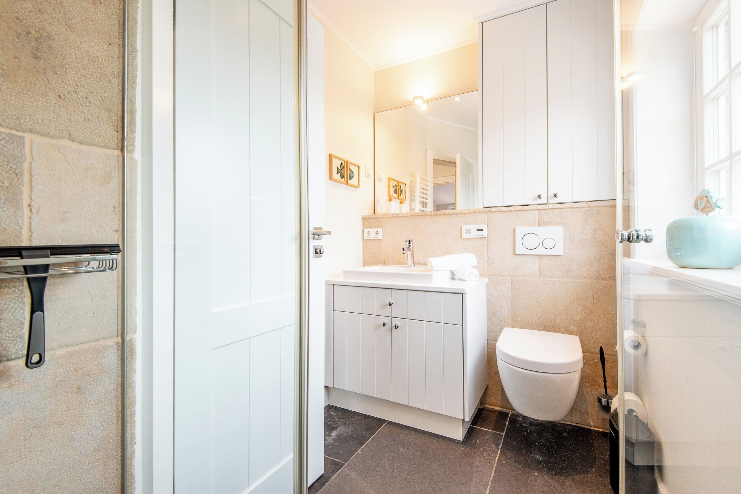 A bathroom with a white sink, toilet, and cabinets, a mirror, and a shower area.