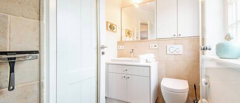 A bathroom with a white sink, toilet, and cabinets, a mirror, and a shower area.